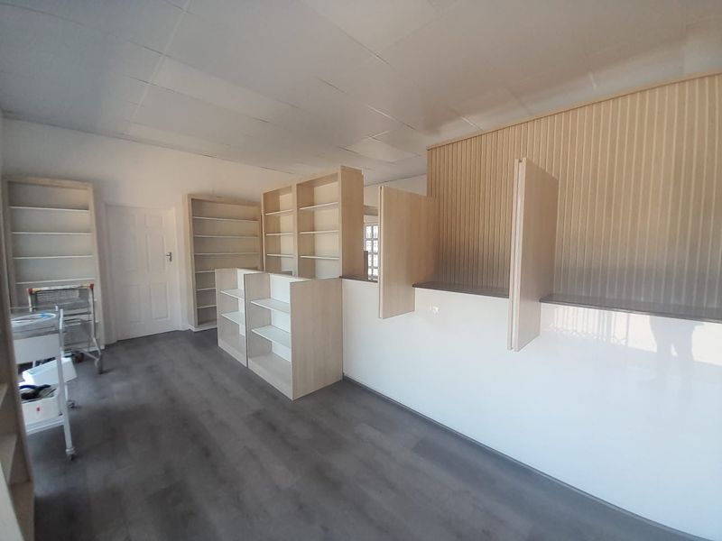 A bright, open-plan retail space featuring modern laminate flooring, built-in shelving units, and a professional service counter with panelled wall detailing.