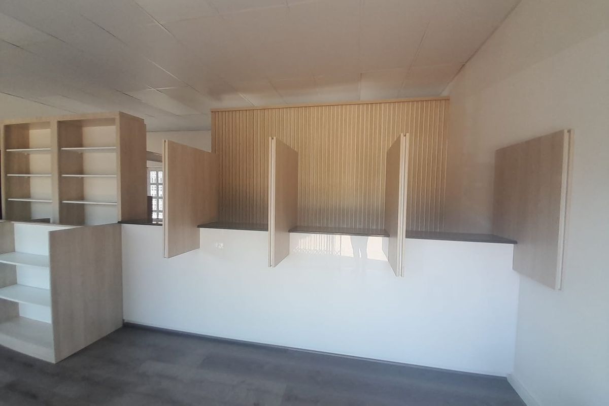 A clean, modern retail space featuring a built-in service counter with privacy dividers, integrated shelving, and contemporary wood-paneled wall accents.