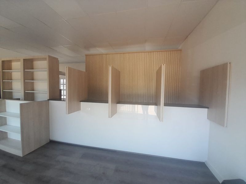 A clean, modern retail space featuring a built-in service counter with privacy dividers, integrated shelving, and contemporary wood-paneled wall accents.