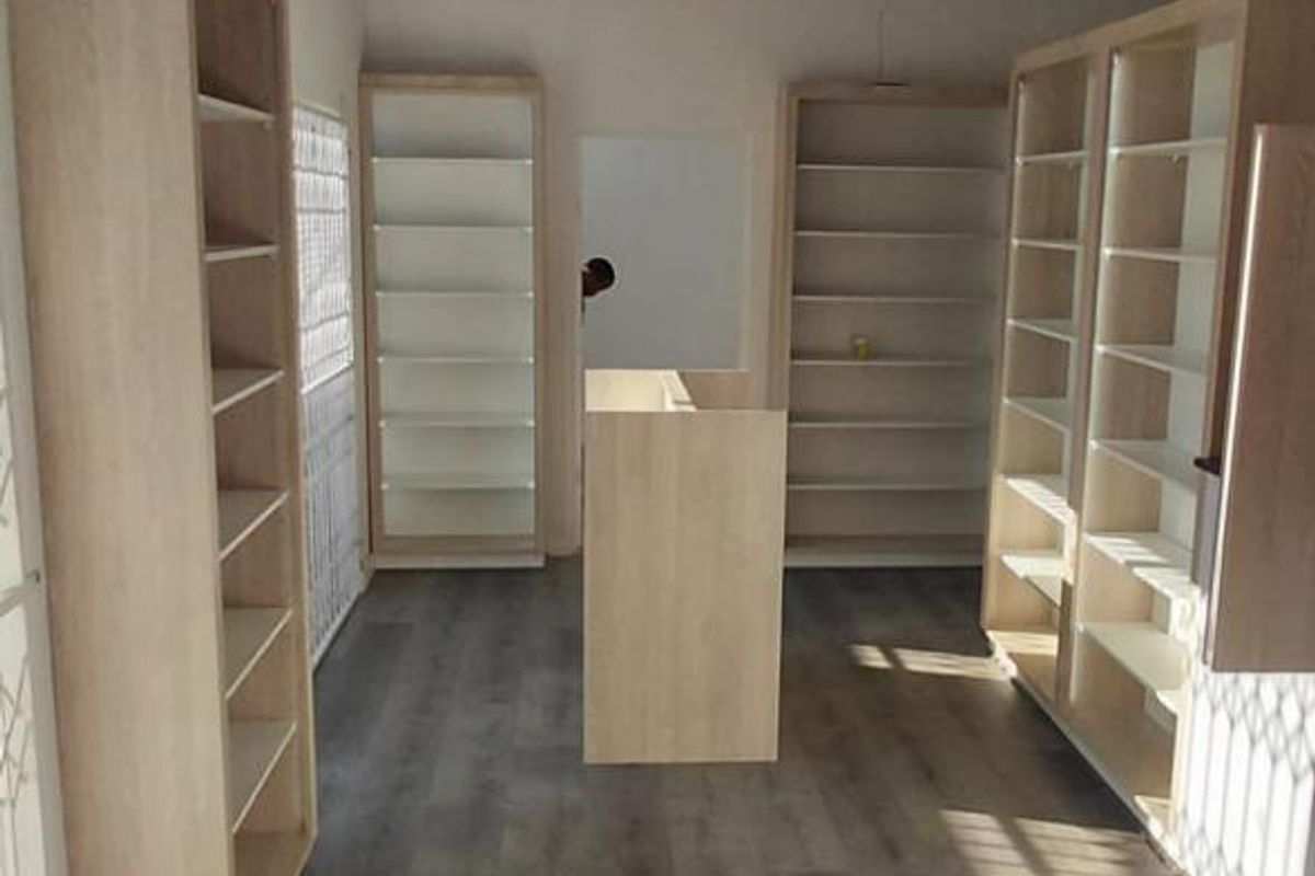 A bright, open retail space featuring modern laminate flooring, built-in shelving units, and a suspended ceiling, suitable for various commercial uses.