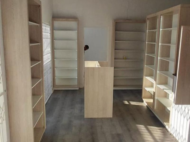 A bright, open retail space featuring modern laminate flooring, built-in shelving units, and a suspended ceiling, suitable for various commercial uses.