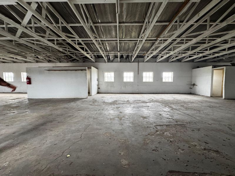 Spacious industrial utility area featuring exposed steel roof trusses, concrete flooring, and multiple windows, offering a versatile open-plan layout for various commercial uses.