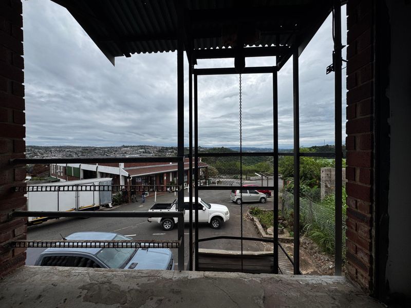 An elevated industrial balcony area featuring exposed brickwork, a corrugated metal roof, and metal safety railings overlooking the property grounds.