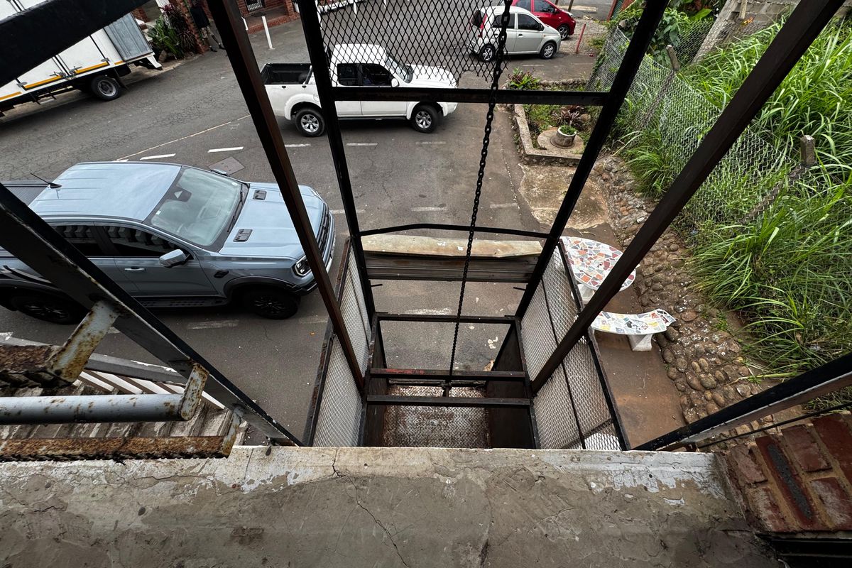 Industrial freight elevator lift with metal mesh enclosure and chain mechanism, showing signs of significant wear and surface corrosion.