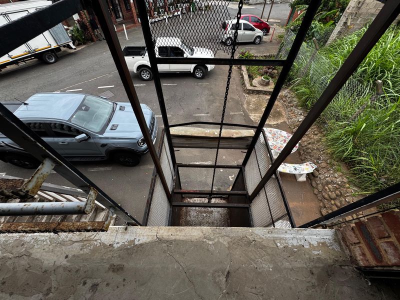 Industrial freight elevator lift with metal mesh enclosure and chain mechanism, showing signs of significant wear and surface corrosion.