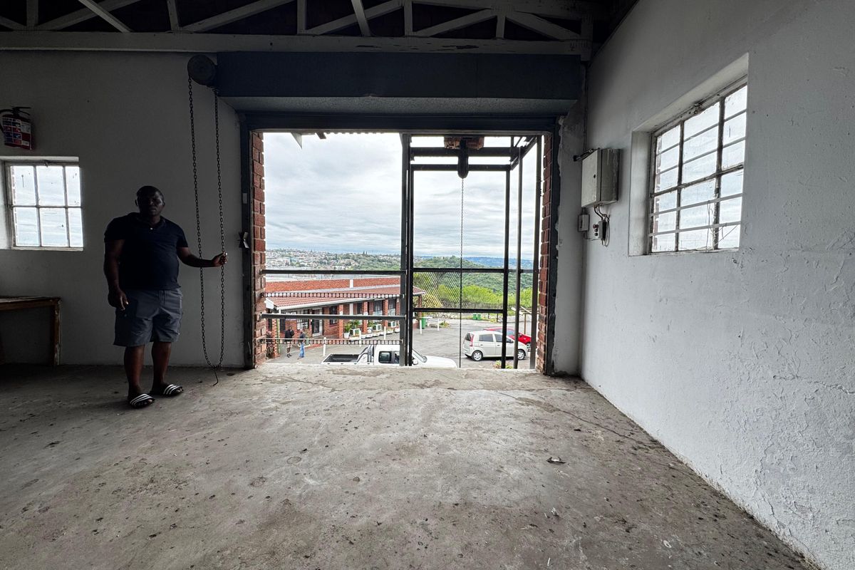 An industrial utility space featuring exposed steel roof trusses, concrete flooring, and a large roller shutter door opening to an exterior view.