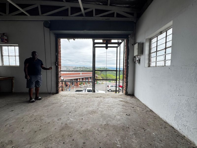An industrial utility space featuring exposed steel roof trusses, concrete flooring, and a large roller shutter door opening to an exterior view.