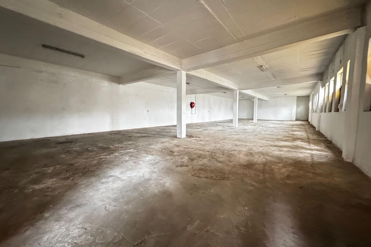 Spacious open-plan industrial warehouse area featuring concrete flooring, exposed structural beams, and functional fire safety equipment.