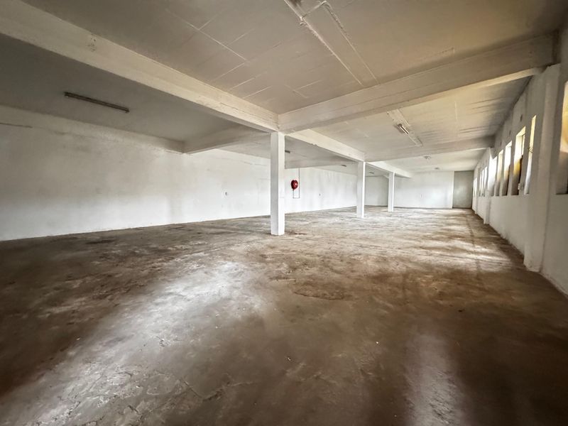 Spacious open-plan industrial warehouse area featuring concrete flooring, exposed structural beams, and functional fire safety equipment.