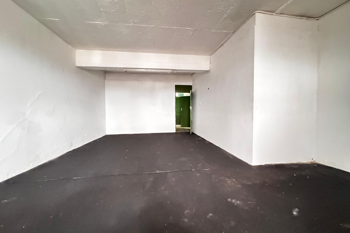An empty industrial utility space featuring exposed concrete ceilings, dark flooring, and a green emergency exit door.