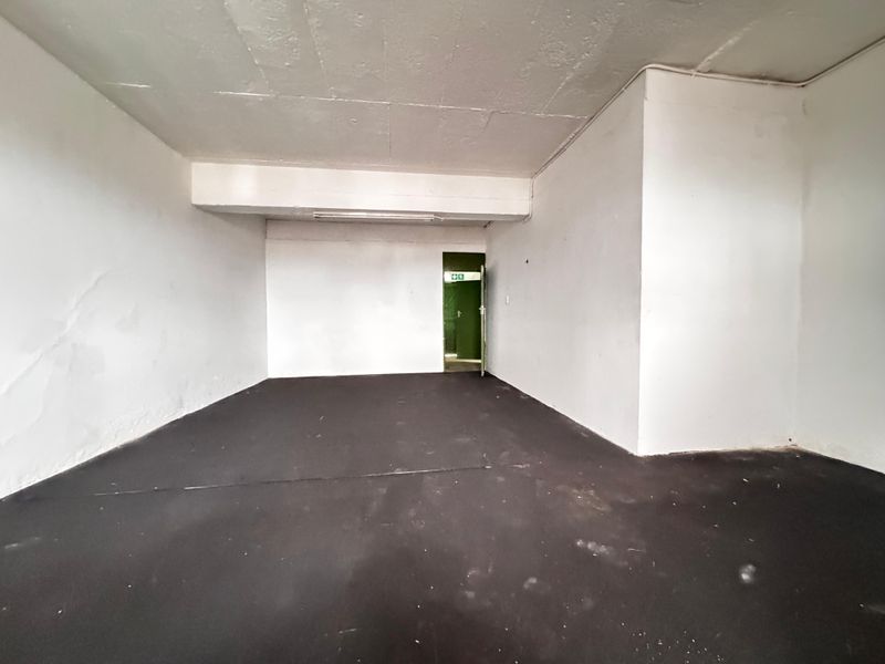 An empty industrial utility space featuring exposed concrete ceilings, dark flooring, and a green emergency exit door.