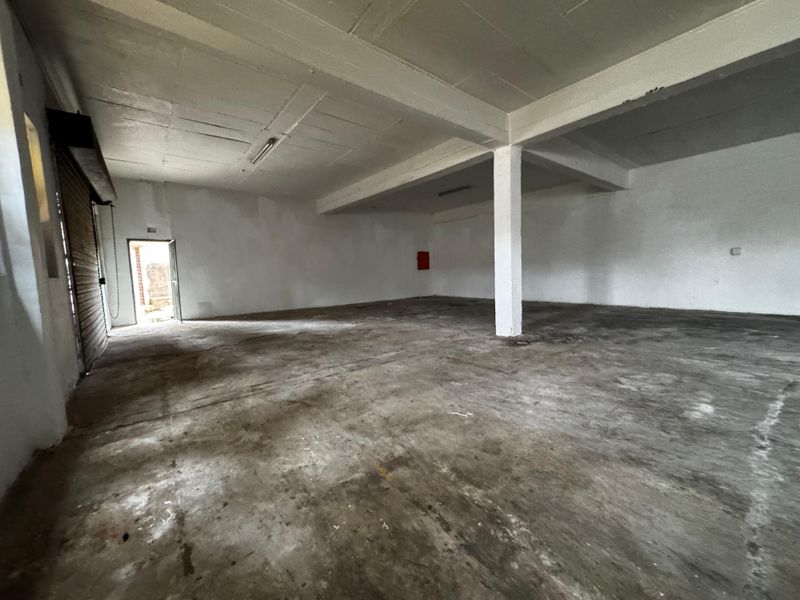 Spacious industrial utility area featuring a concrete floor, exposed ceiling, structural support column, and a roller shutter door, suitable for storage or workshop use.