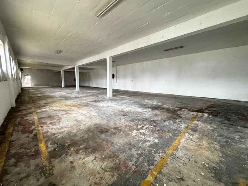 A large, open-plan industrial utility space featuring concrete flooring, structural support columns, and overhead fluorescent lighting, suitable for storage or workshop use.