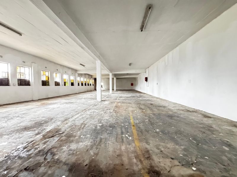 Expansive industrial utility space featuring high ceilings, concrete flooring, support columns, and multiple windows, suitable for storage or workshop use.