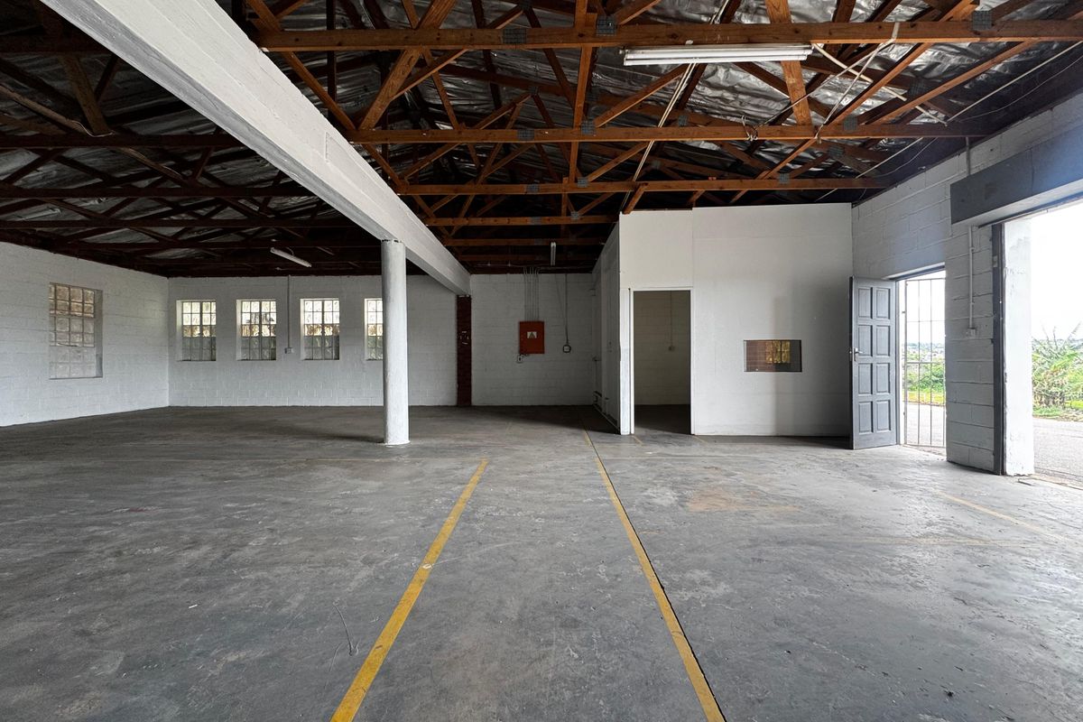 Spacious industrial utility area featuring exposed timber roof trusses, concrete flooring, and painted block walls, suitable for workshop or storage use.