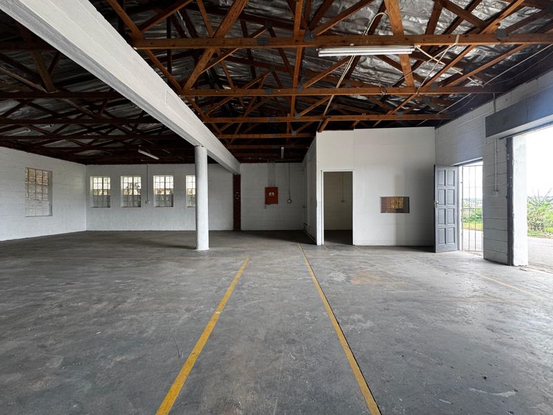 Spacious industrial utility area featuring exposed timber roof trusses, concrete flooring, and painted block walls, suitable for workshop or storage use.