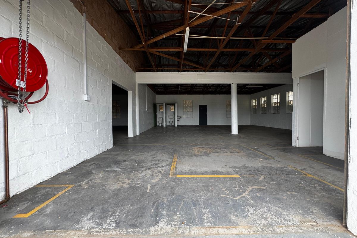 Spacious industrial utility area featuring exposed timber roof trusses, concrete flooring, and integrated toilet facilities, suitable for various commercial or storage applications.