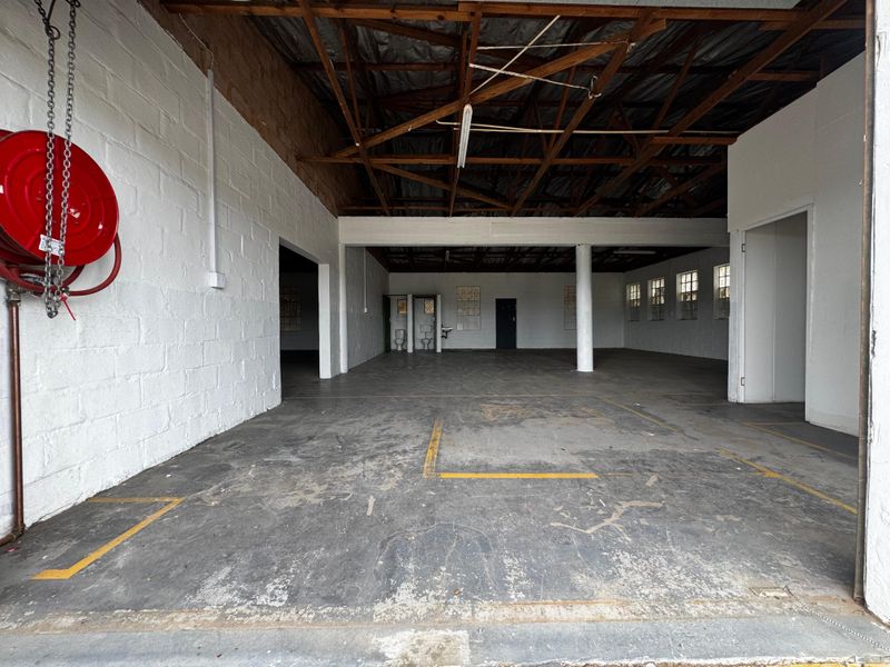 Spacious industrial utility area featuring exposed timber roof trusses, concrete flooring, and integrated toilet facilities, suitable for various commercial or storage applications.