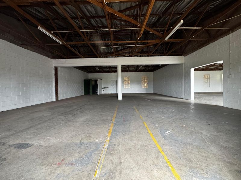 Spacious industrial utility area featuring exposed timber roof trusses, concrete flooring, and painted block walls, suitable for storage or workshop use.