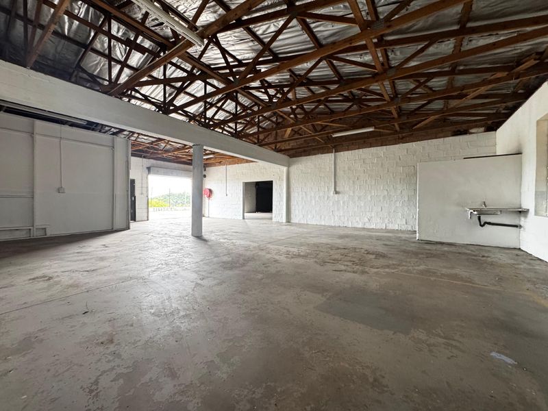 Spacious industrial utility area featuring exposed timber roof trusses, concrete flooring, painted brick walls, and a wall-mounted utility sink.