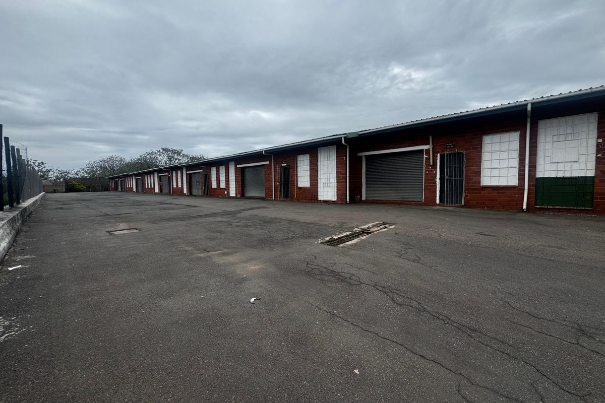 Industrial complex featuring multiple units with roller shutter doors, security gates, and a large asphalt yard area.