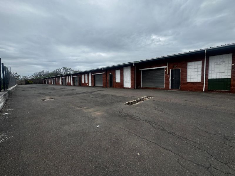 Industrial complex featuring multiple units with roller shutter doors, security gates, and a large asphalt yard area.