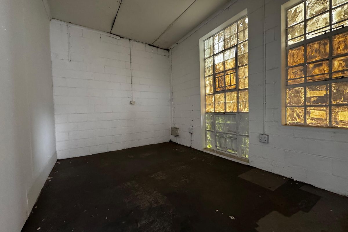 An empty industrial utility space featuring exposed concrete block walls, concrete flooring, and large steel-framed windows providing natural light.