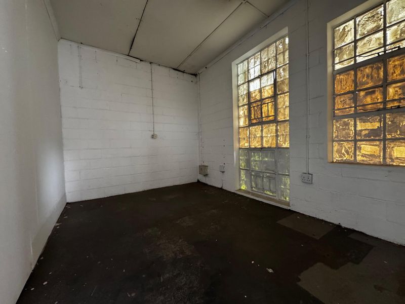 An empty industrial utility space featuring exposed concrete block walls, concrete flooring, and large steel-framed windows providing natural light.