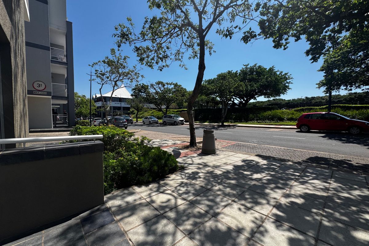 A clear street-level view showing the paved sidewalk, landscaped verge, and building exterior in a well-maintained retail or commercial area.