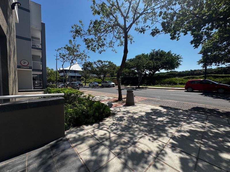 A clear street-level view showing the paved sidewalk, landscaped verge, and building exterior in a well-maintained retail or commercial area.