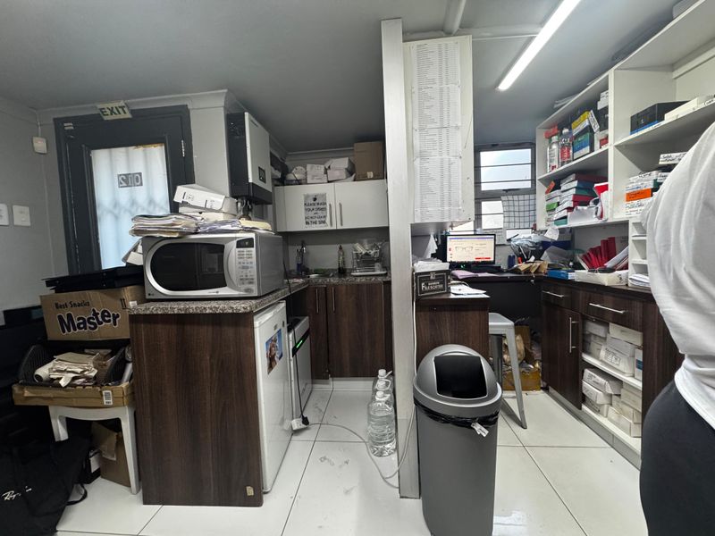 A functional scullery or utility area featuring built-in cabinetry, laminate countertops, a sink, and tiled flooring, currently utilized for storage and workspace.