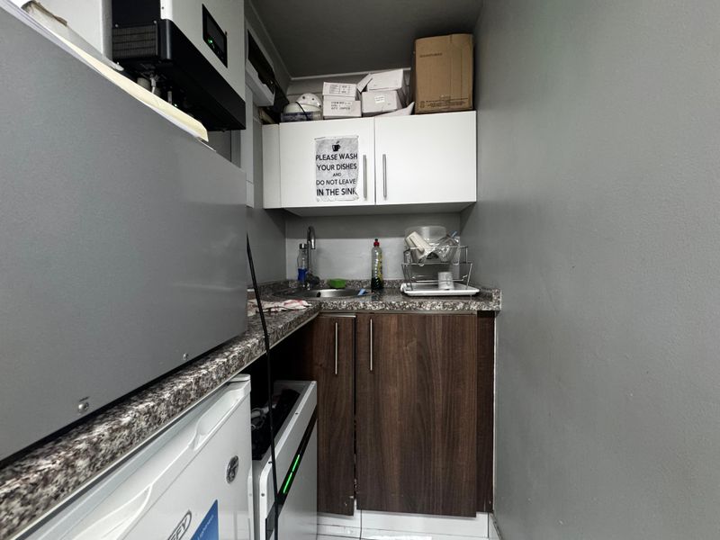 A compact scullery or kitchenette area featuring built-in cabinetry, a laminate countertop, and a stainless steel sink.
