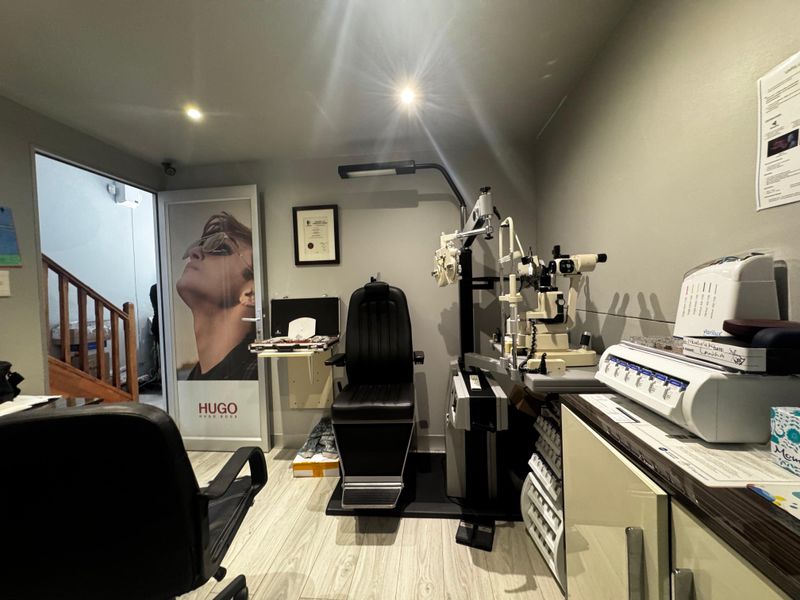 A professional optometry examination room featuring specialized diagnostic equipment, built-in cabinetry, and modern laminate flooring.