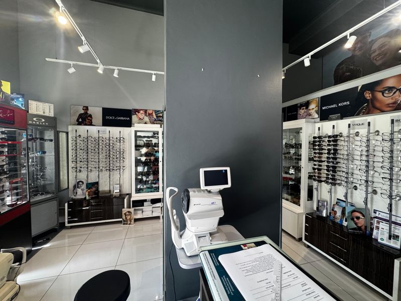 A well-maintained retail optical store interior featuring professional track lighting, tiled flooring, and extensive built-in wall-mounted eyewear display cabinetry.