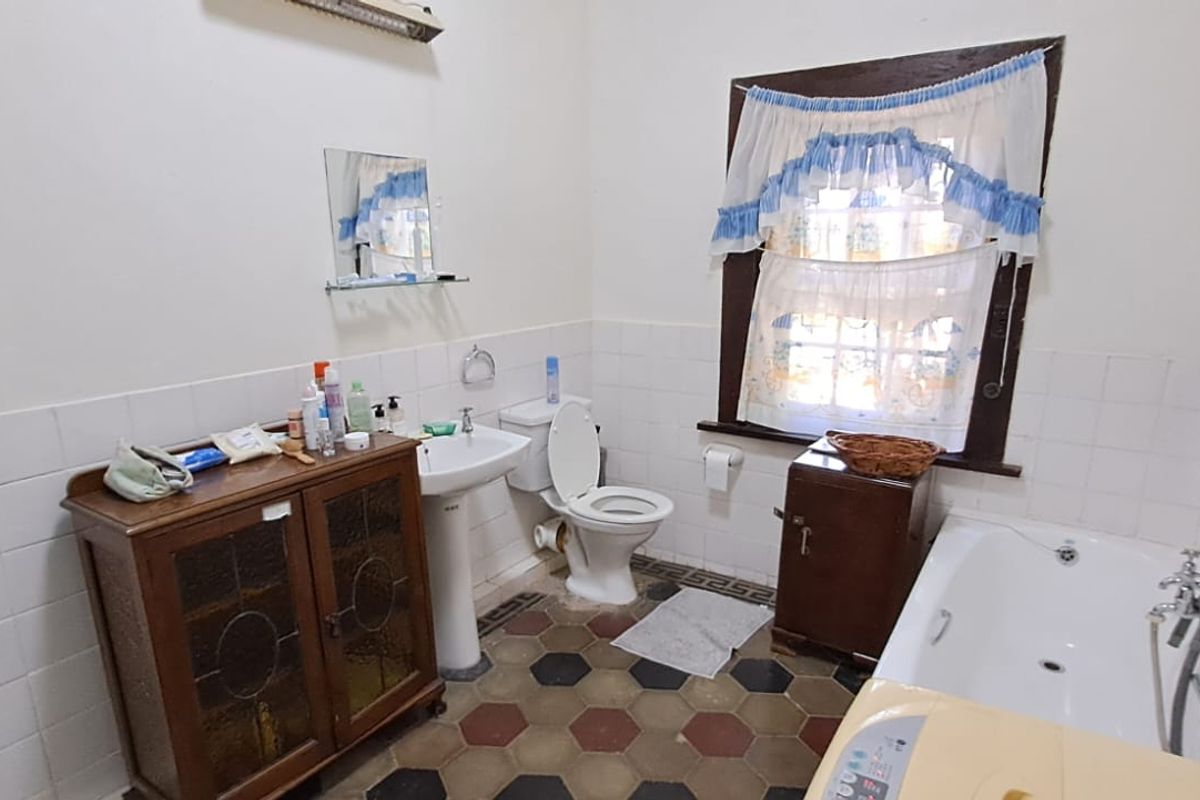 A dated bathroom featuring a pedestal basin, toilet, and bathtub with classic hexagonal floor tiles and wall tiling.