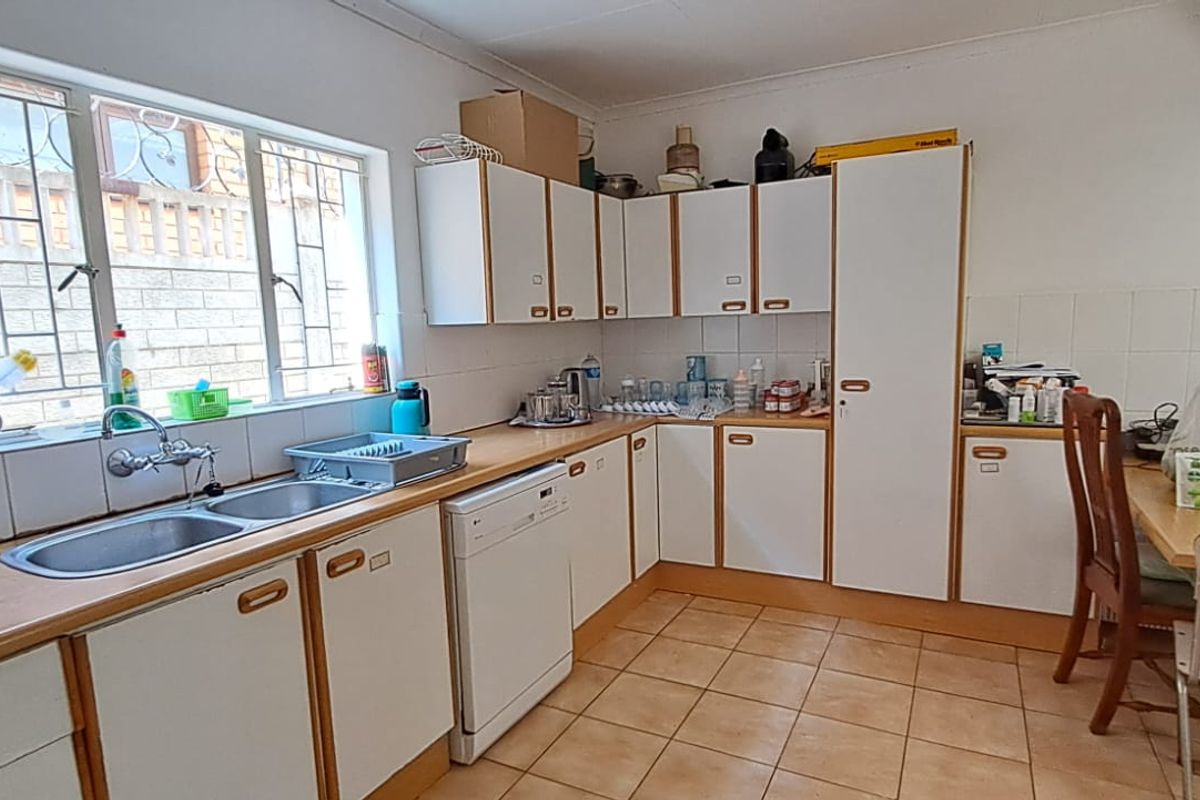 A functional kitchen featuring laminate countertops, double basin sink, tiled splashback, and ample built-in cabinetry with tiled flooring.
