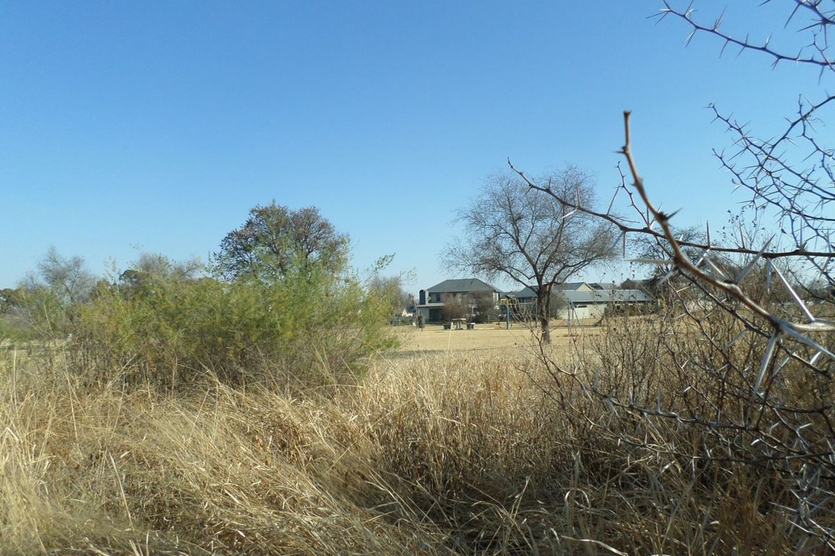 A view of a vacant residential plot featuring dry grass and native vegetation with neighboring properties visible in the distance.