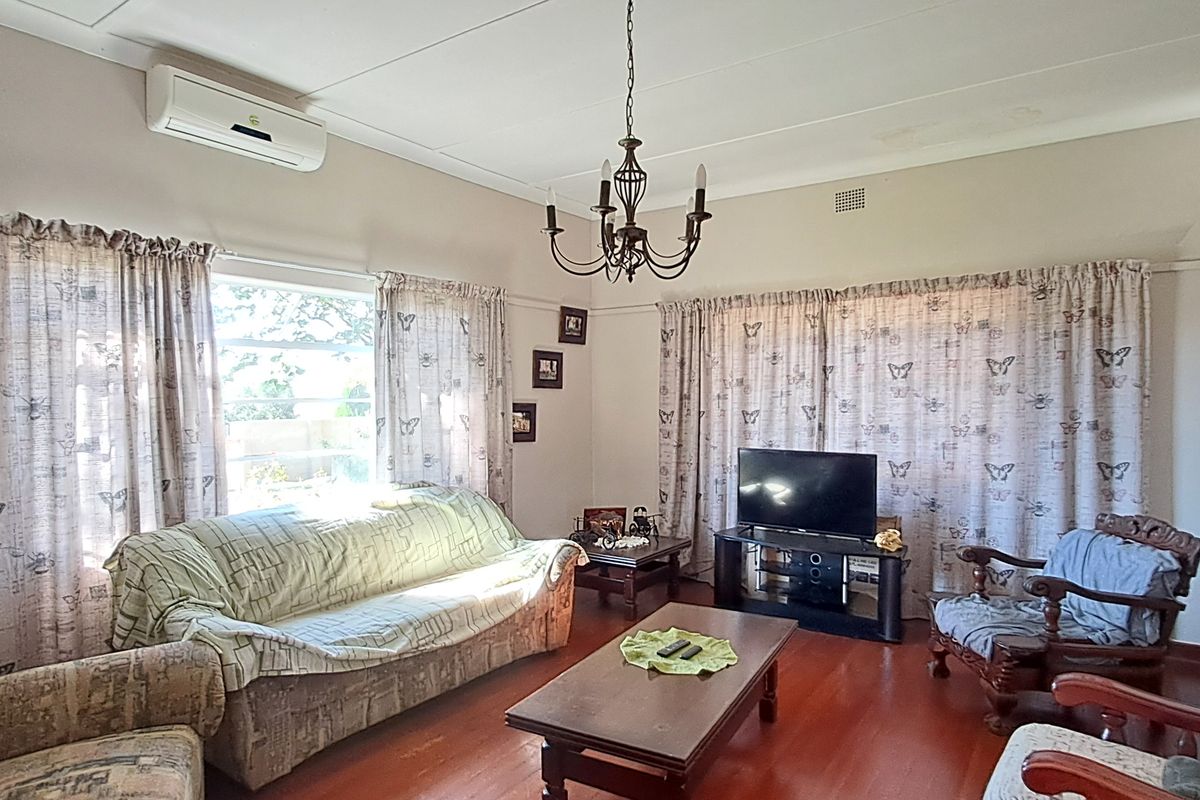 A comfortable living room featuring hardwood flooring, a coved ceiling with a decorative chandelier, and a wall-mounted split-system air conditioner.
