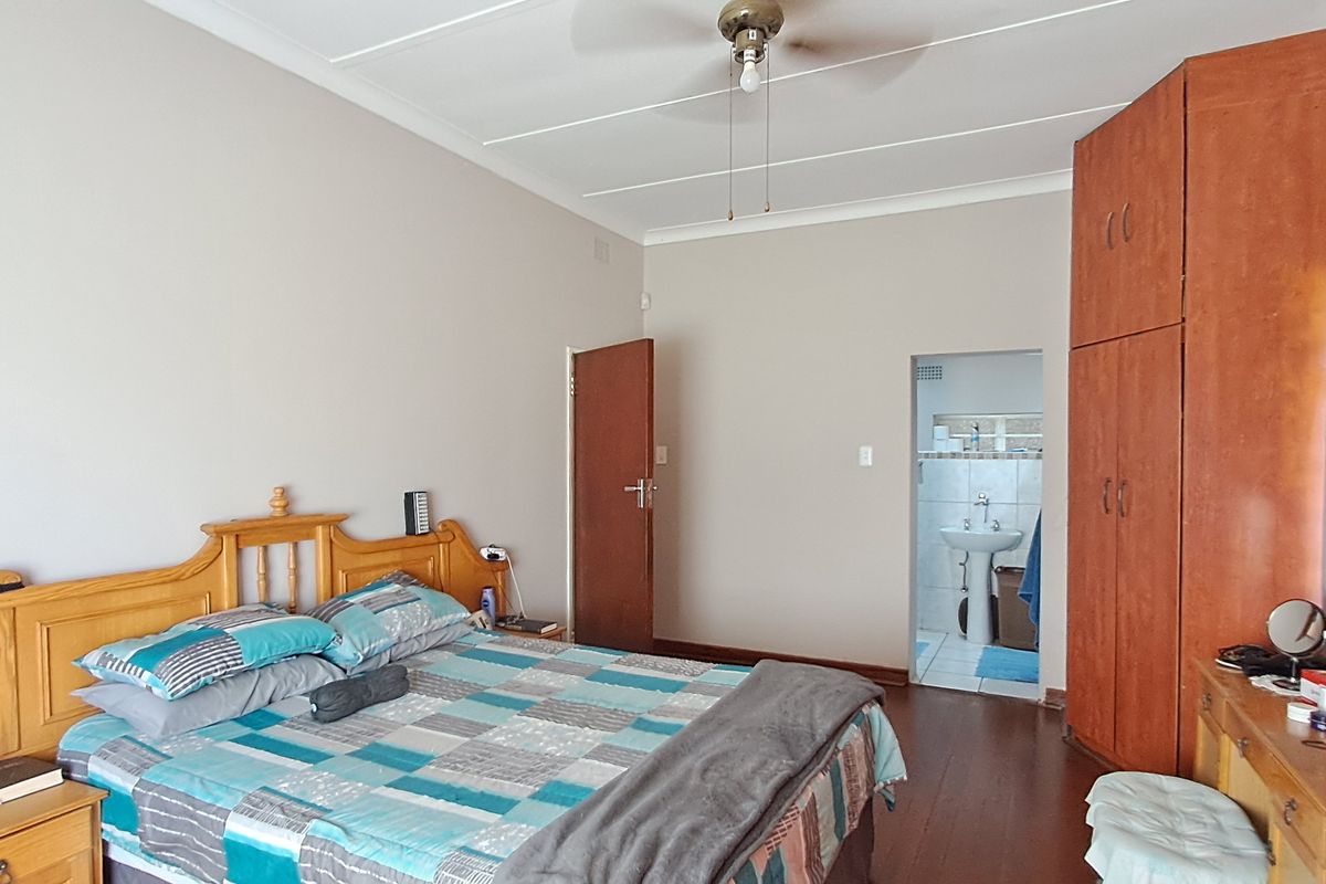 A bedroom featuring built-in wooden cupboards, hardwood flooring, a ceiling fan, and direct access to an en-suite bathroom.