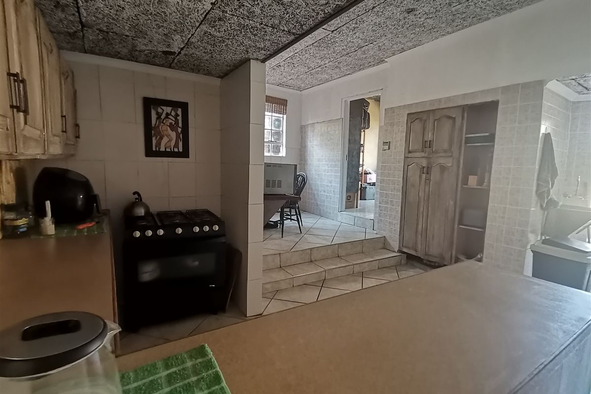 A dated kitchen featuring built-in cabinetry, a gas stove, and tiled finishes, with a split-level layout leading to an adjacent room.