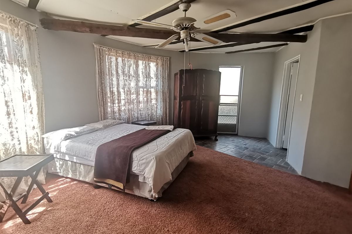 Spacious bedroom featuring exposed timber ceiling beams, a ceiling fan, and a combination of carpeted and tiled flooring with direct access to an exterior door.