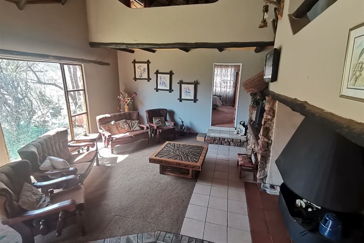 Spacious living room featuring a high thatched ceiling with exposed timber beams, a prominent stone-clad fireplace, and large windows providing natural light.