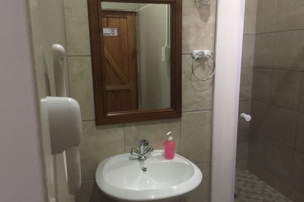 A functional bathroom featuring a pedestal basin with chrome mixer tap, wall-mounted mirror, and a tiled shower enclosure with neutral wall finishes.
