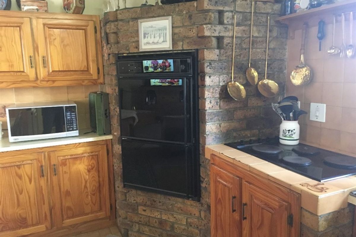 A rustic kitchen featuring a prominent brick chimney breast, built-in double oven, electric cooktop, and traditional wooden cabinetry with tiled splashbacks.