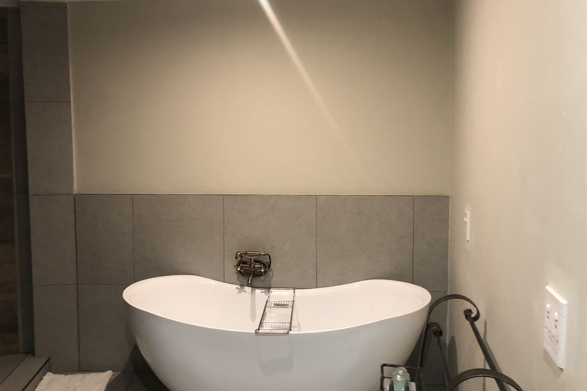 A modern bathroom featuring a sleek freestanding bathtub with a wall-mounted mixer and neutral grey tiled splashback.