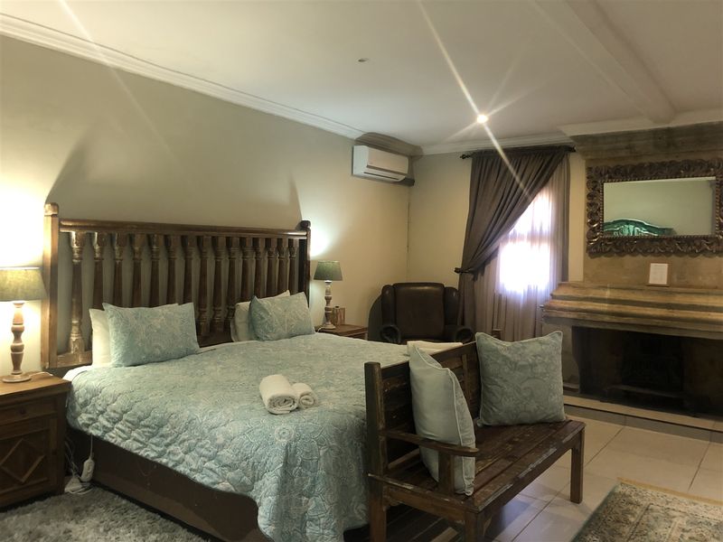 Spacious bedroom featuring a stone fireplace, crown molding, and a wall-mounted air conditioning unit with tiled flooring.