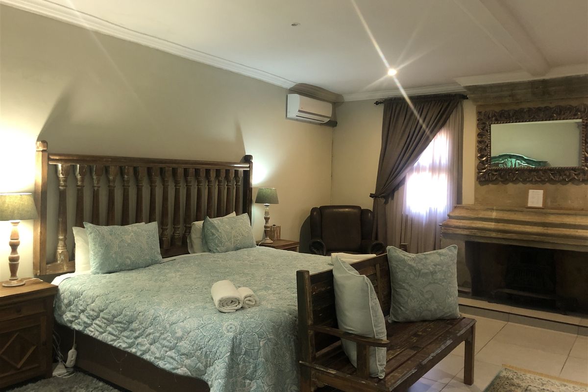 Spacious bedroom featuring a stone fireplace, crown molding, and a wall-mounted air conditioning unit with tiled flooring.