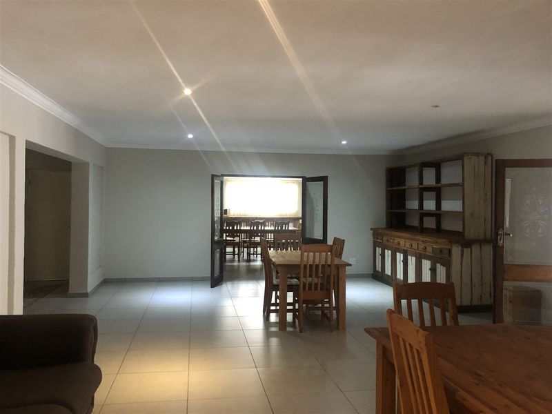 Spacious open-plan living and dining area featuring neutral tiled flooring, recessed lighting, and double doors leading to an adjacent room.