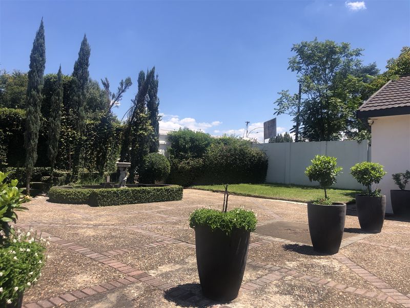 A well-maintained garden featuring a paved courtyard, stone fountain, mature trees, and perimeter walling, providing a private outdoor space.