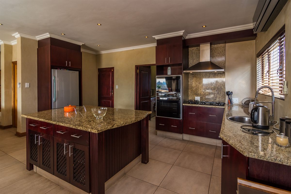 Spacious kitchen featuring dark wood cabinetry, granite countertops, a central island, and built-in appliances, finished with neutral tiled flooring and recessed lighting.